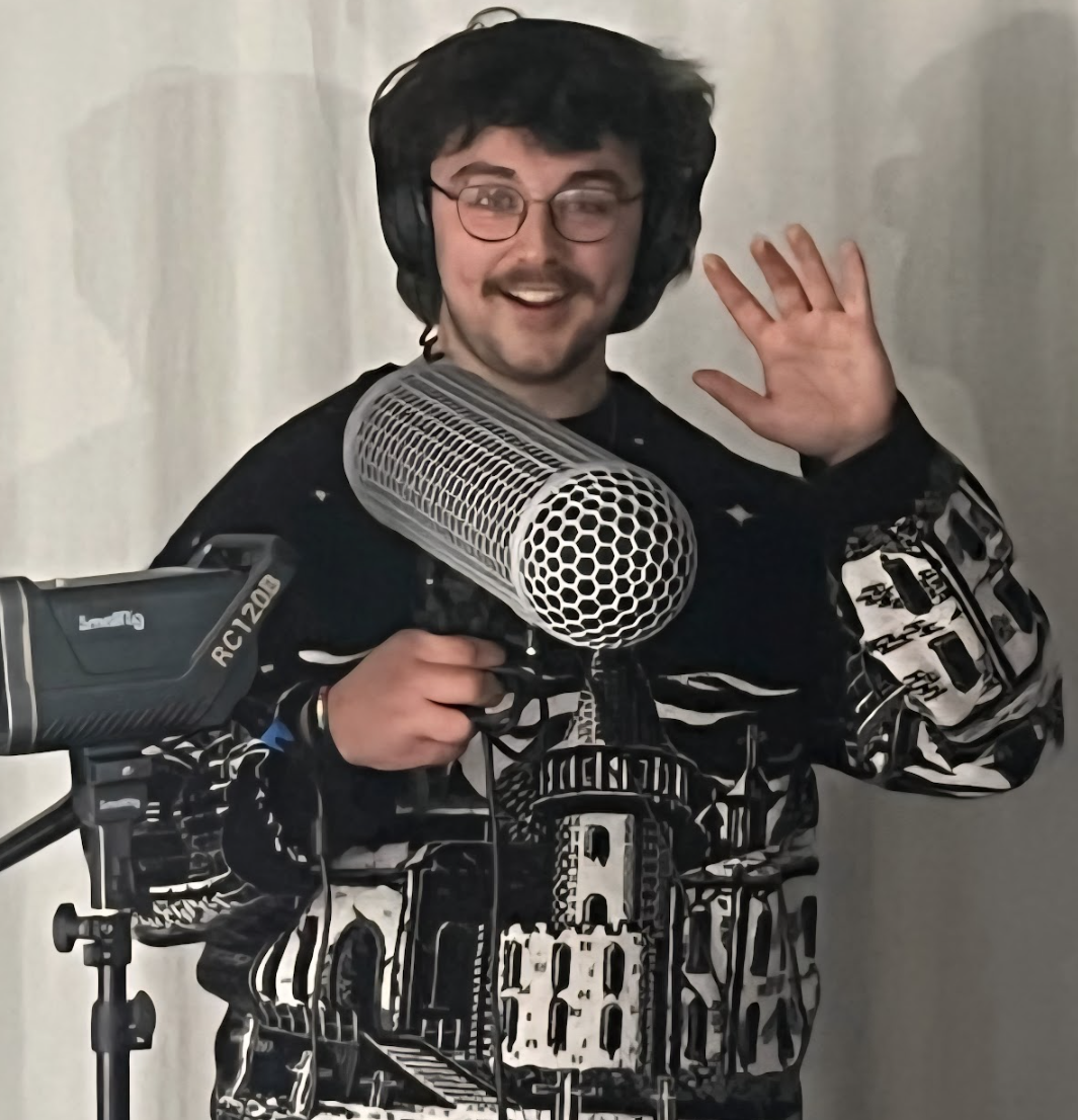 Chris Gray holding a big microphone and waving to the camera with a friendly greeting expression